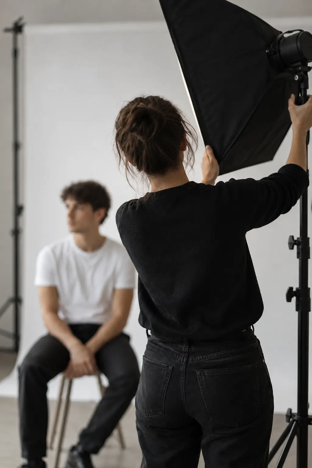 Fotógrafa ajustando un softbox para la foto tamaño credencial de un joven frente a un fondo blanco
